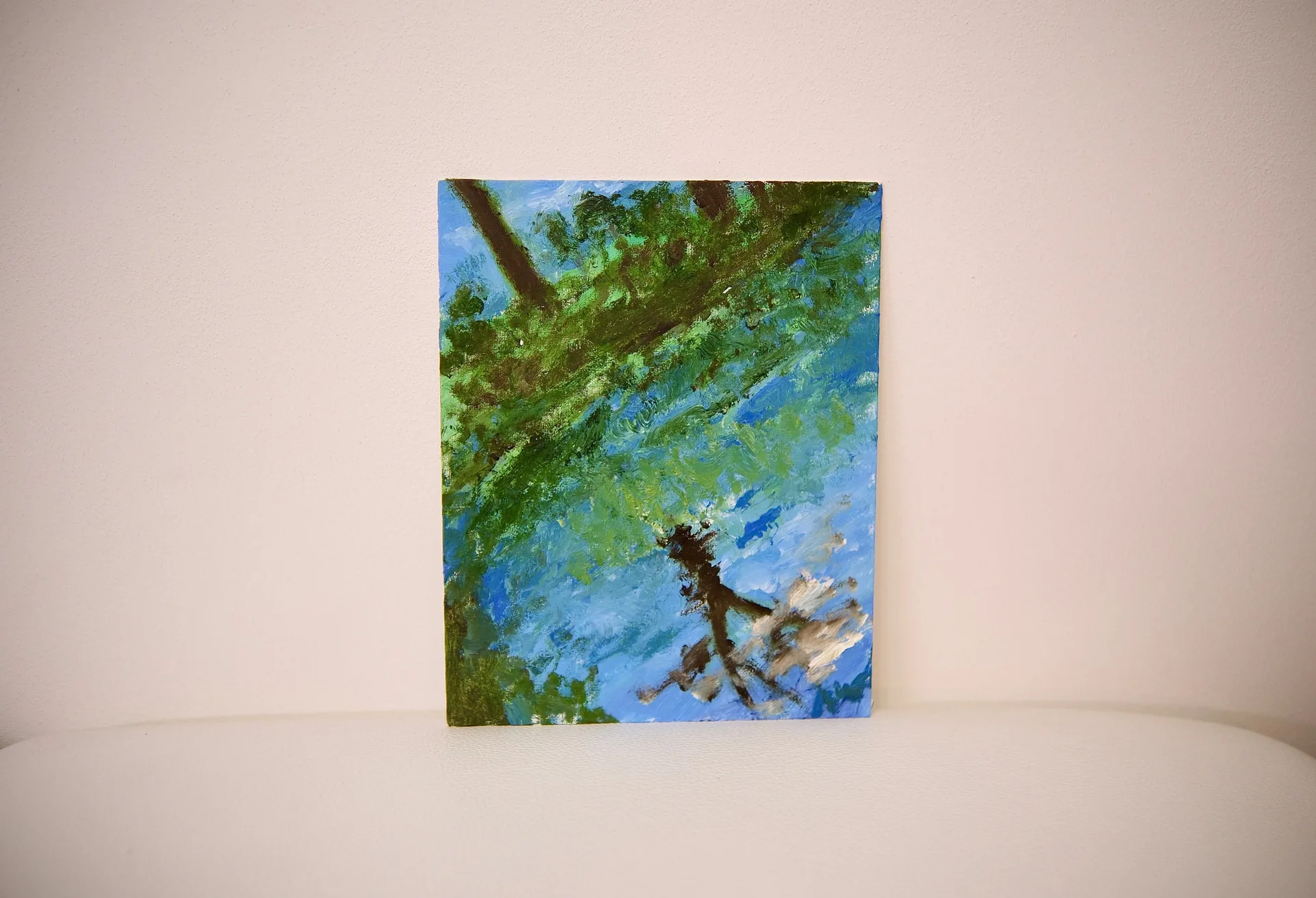 The unframed canvas propped against a warm off-white wall, its green branch and rippled blue water seen straight on.