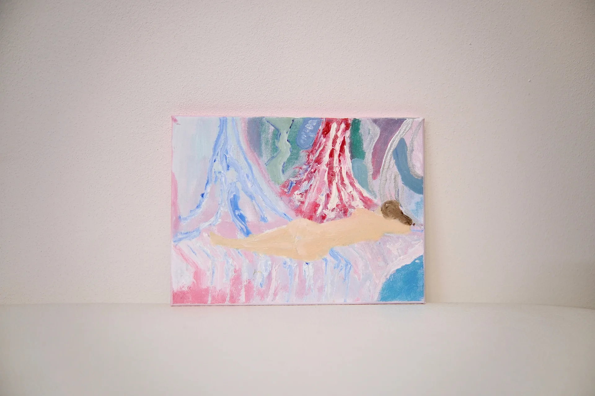 The unframed canvas leaning against a pale wall, its reclining pale figure set against streaming pink and blue.