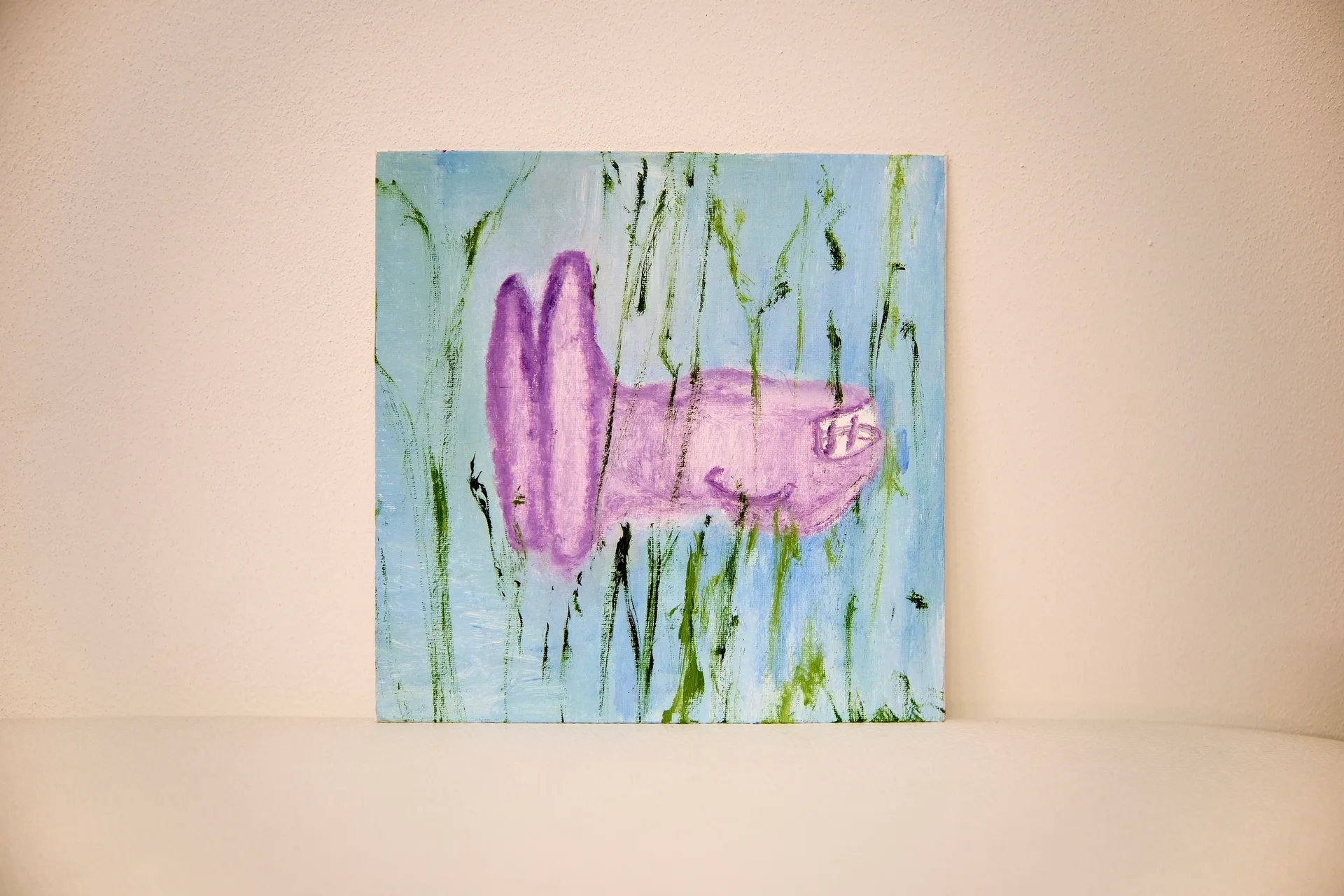 The square canvas propped against a pale wall, its lilac vehicle shape floating among green strokes on pale blue.