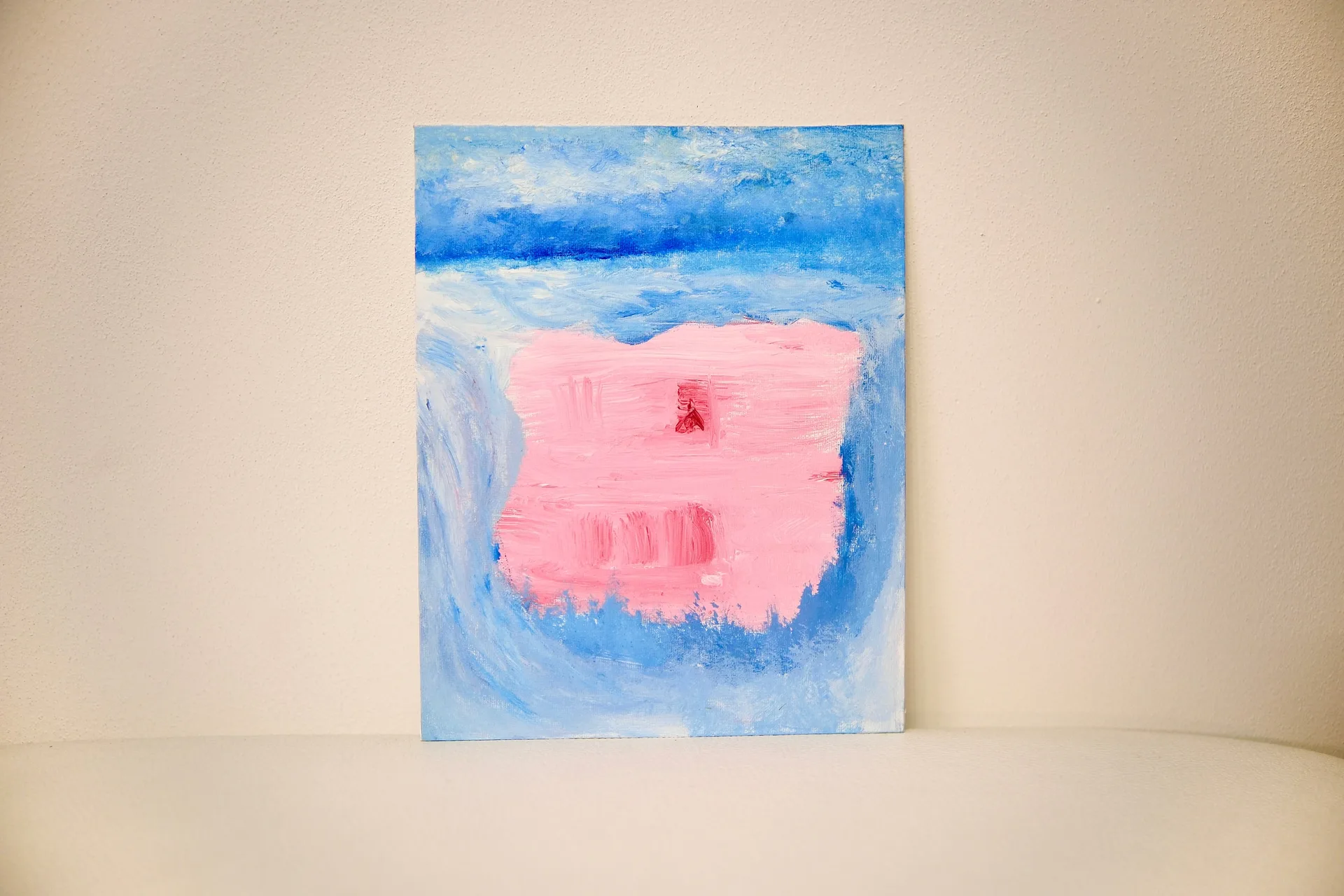 The unframed canvas propped against a warm off-white wall, the pink block glowing at the centre of its blue field.